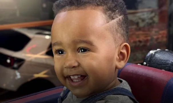 Bebê sorrindo na cadeira com cabelo curto e um risco na lateral