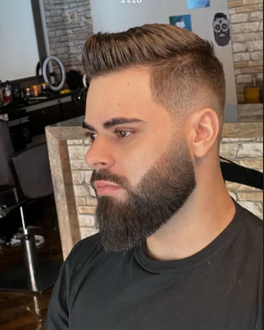 Cliente de perfil com degradê na lateral, topete penteado e barba cheia desenhada