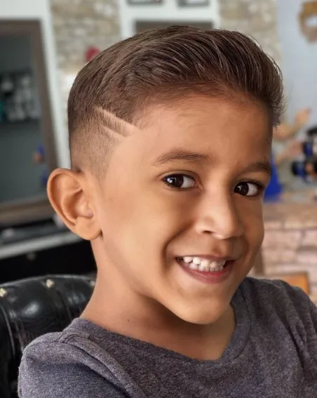 Menino sorrindo com degradê baixo, topete e dois riscos na lateral